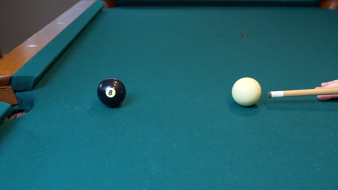A Caucasion person setting up, and making, a billiards shot of the eight ball in the side pocket