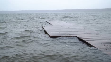 wide shot of the lake waves splash jumping over a wooden deck in cloudy autumn day