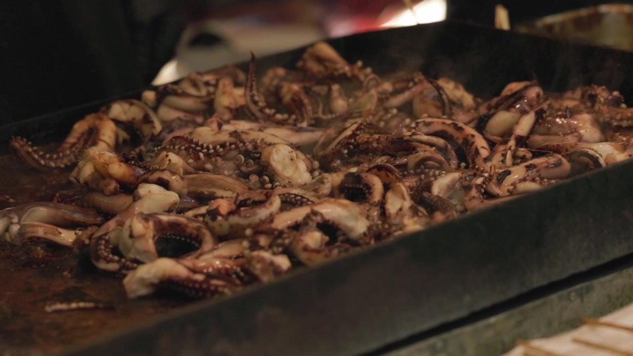 Polipetti grigliati su una piastra nelle bancarelle di street food. - Primo piano.