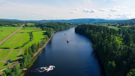 Aerial-view-of-tourist-resort-Järvsö,-Sweden-with-boats-and-jetski-moving-down-river-in-summer-sun