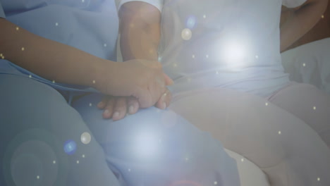 spots of light against mid section of health worker holding patients hand