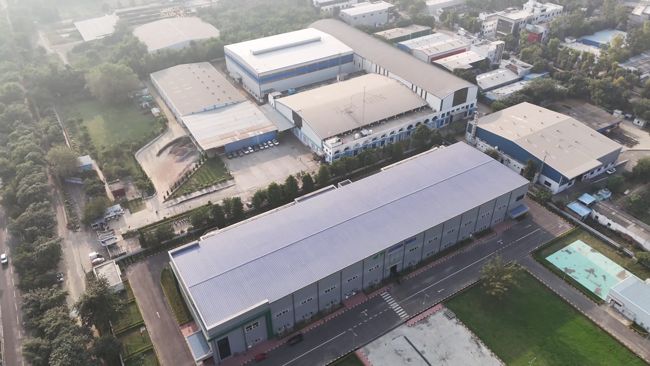Wide aerial shot of a modern warehouse facility, emphasizing renewable power generation, large-scale industry, and sustainability within a landscaped industrial campus.
