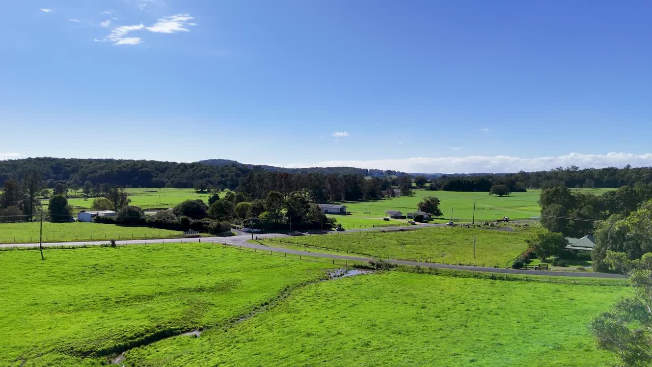 Aerial footage of lush green fields and distant hills under clear blue skies in Bellingen, NSW, Australia