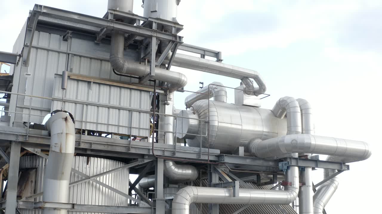 Aerial view showing large industrial storage tanks, pipelines, and factory structures, slight upward camera movement, Castets, France