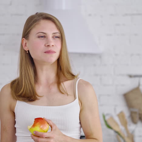 half-length portrait of young woman with apple. beautiful girl is eating a fresh organic fruit in the kitchen. healthy food. dieting concept.