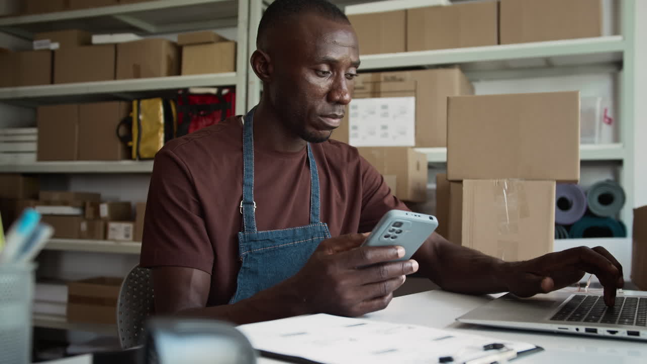 African American Manager Using Smartphone when Filling Parcel Data at Storehouse