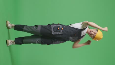 cuerpo lleno de trabajadora asiática que usa gafas de protección y casco de seguridad cantando y bailando mientras está de pie en el estudio de fondo de la pantalla verde