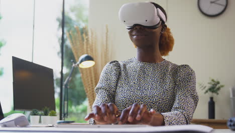 Low-Angle-Shot-Of-Woman-Working-From-Home-Office-At-Desk-Wearing-VR-Headset-Using-AR-Technology