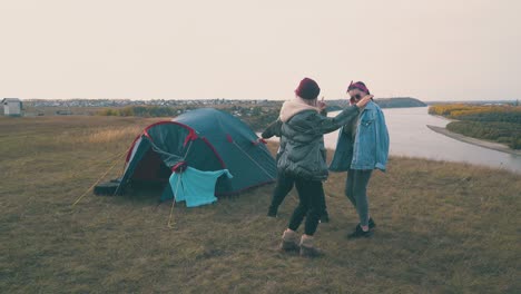 joyful women dance at blue tent on green hill top at sunset