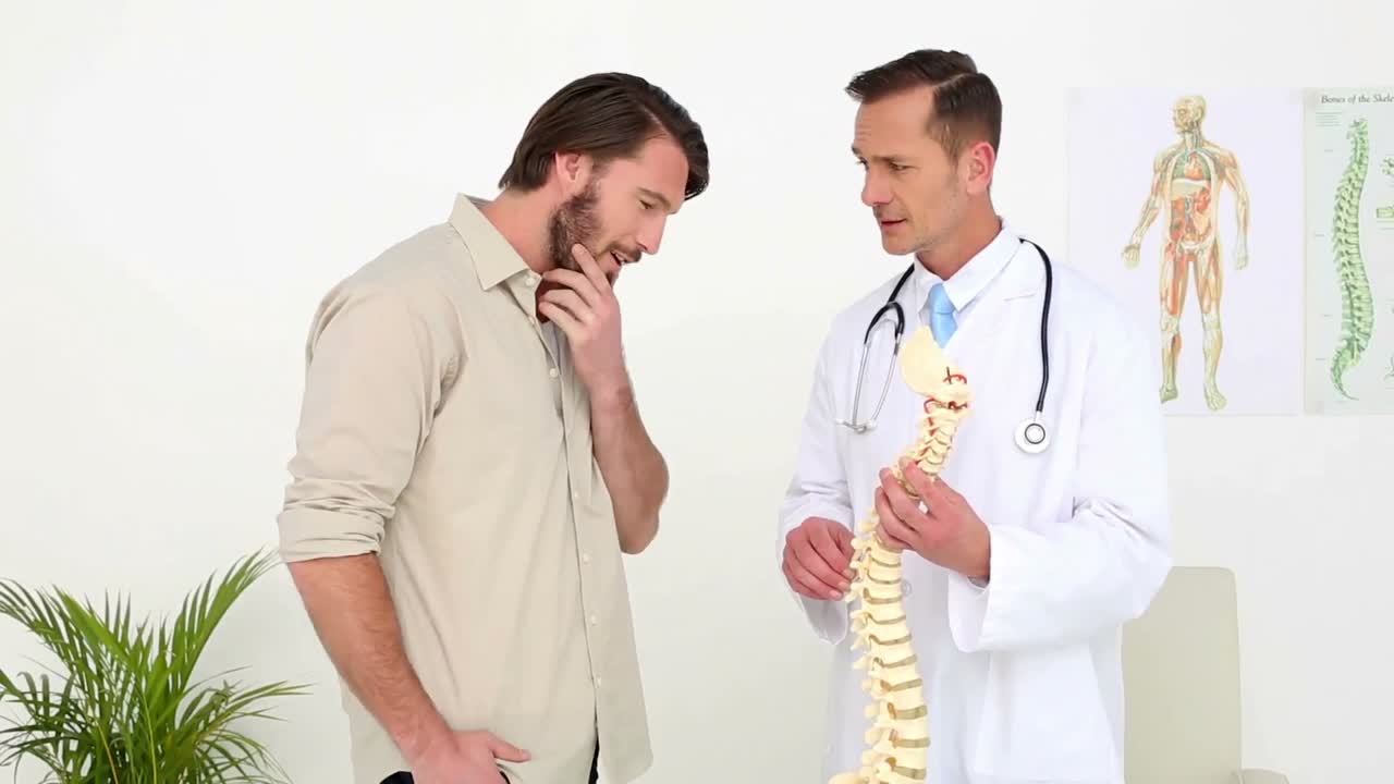 médico hablando con su paciente sobre un modelo de columna vertebral esquelético