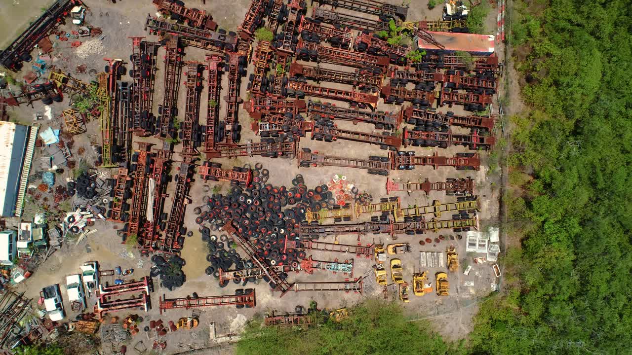 Large junk scrap yard with rusted gutted container boat shipping pieces and tires, drone rises above, bird's eye view