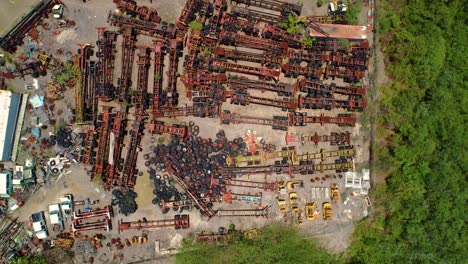 large junk scrap yard with rusted gutted container boat shipping pieces and tires, drone rises above, bird's eye view