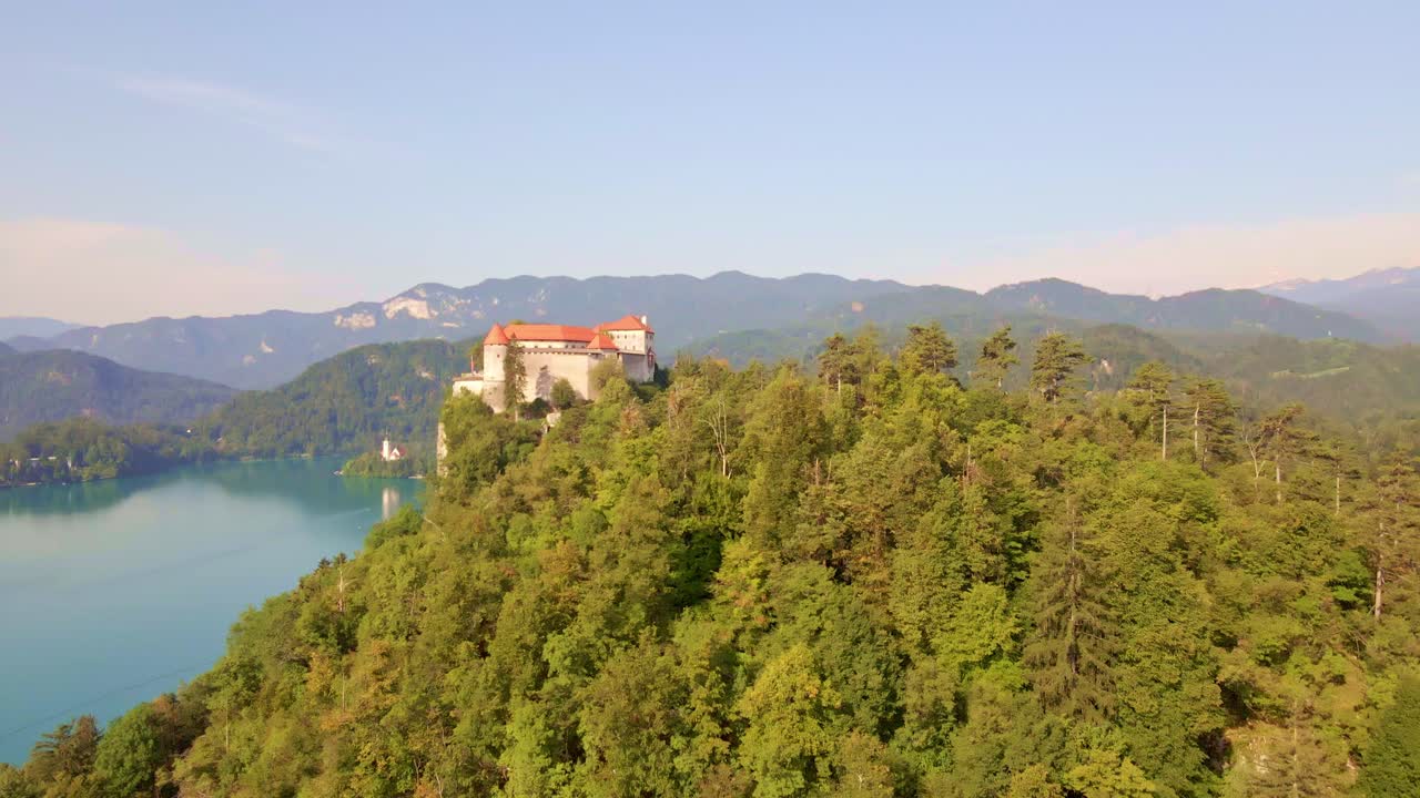 Ripresa aerea fluida con dolly-in cinematografico per rivelare il Castello di Bled che si affaccia sul Lago di Bled, in alto nelle Alpi Giulie in Slovenia.