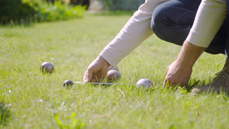 zijaanzicht van een blanke jonge man die de afstand tussen petanqueballen in het park berekent