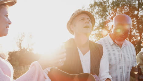 group of mature friends around fire as they drink and sing songs at outdoor campsite