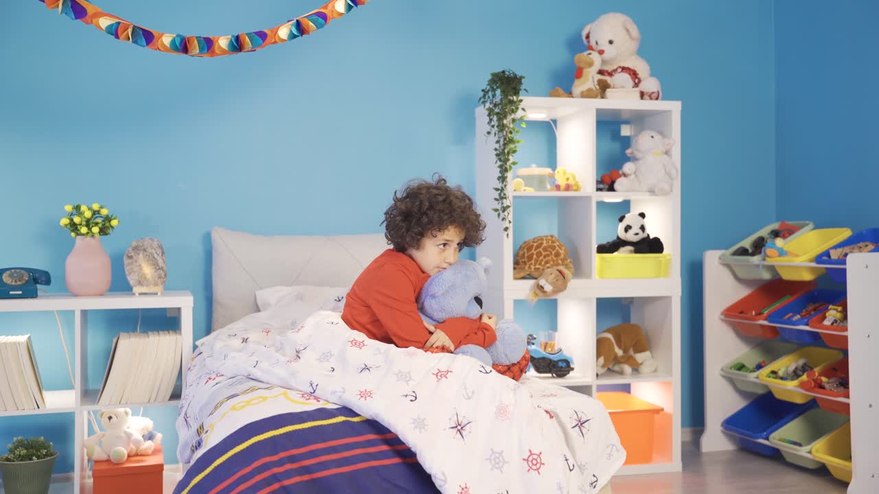 슬픈 우울한 소년이 침대에서 테디 베어를 안아주고 있습니다.