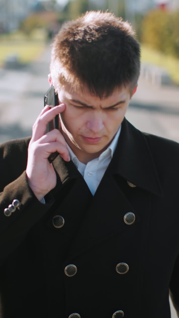 검은 코트를 입은 은행가,  에 전화를 들고, 통화를 할 때 하고, 사려 깊은 모습을 보이고, 현대적인 유리 건물, 부드러운 빛, 나무, 포장된 경로와 함께 도시 환경