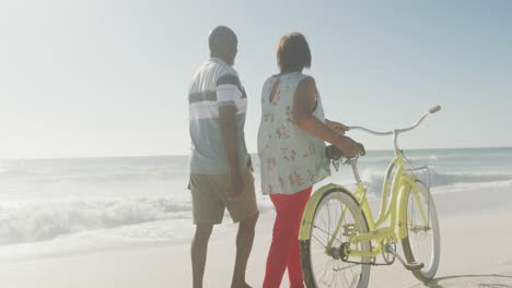 Pareja-Afroamericana-De-Alto-Rango-Caminando-Con-Bicicleta-En-La-Playa-Soleada