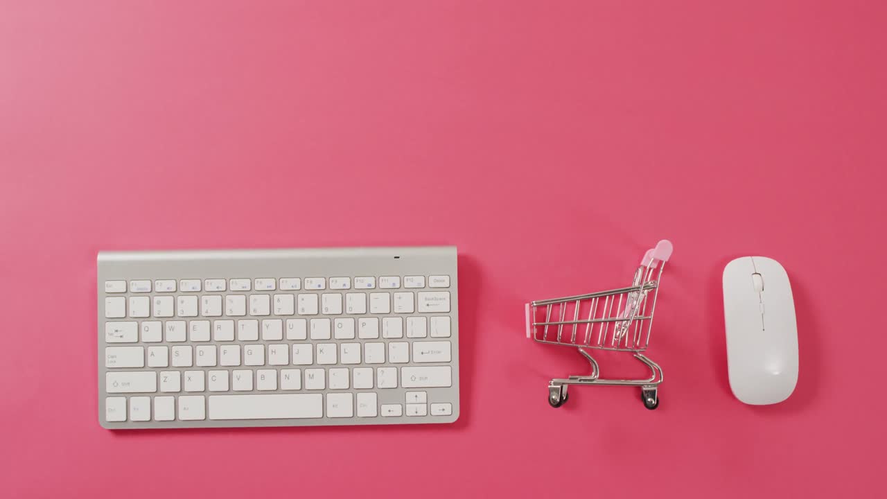 vista aérea del teclado de la computadora, el carrito de compras y el ratón en fondo rosa con espacio de copia