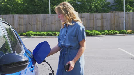 woman charging electric car with cable using app on phone to monitor battery level