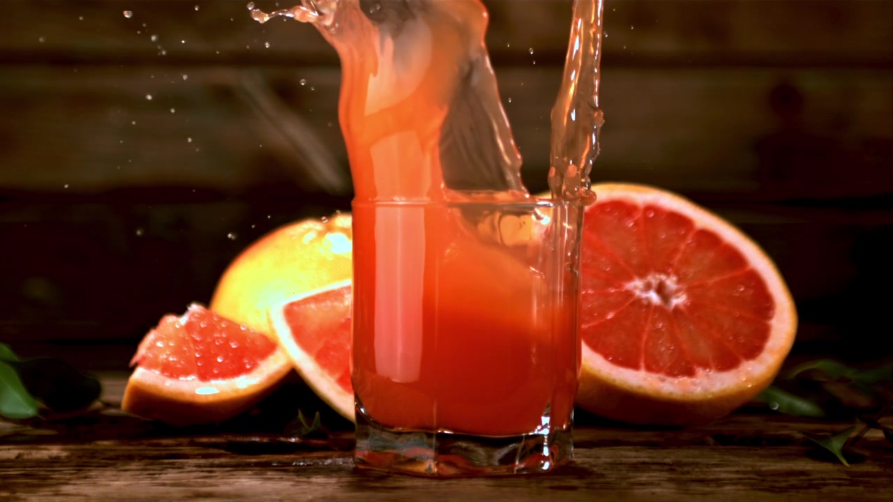 Fetta di pompelmo che si tuffa in un bicchiere di succo fresco.