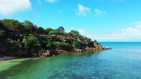 beach bungalows over rocky coast of tropical island washed by calm clear water of turquoise lagoon with coral reefs in malaysia