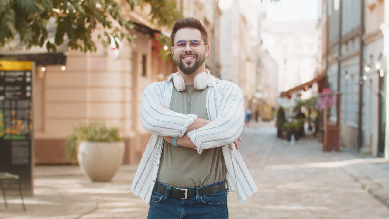 Portrait of happy caucasian young man turning looking at camera standing arms crossed on street