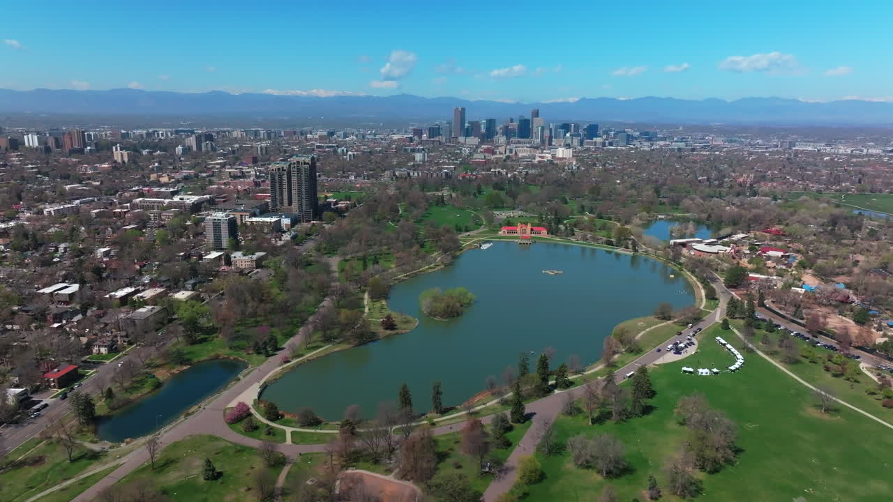 Early spring snowcapped Rocky Mountains downtown Denver City Park cityscape aerial drone Colorado green lush grass Ferril Duck Lake sunny blue skies morning skyscrapers neighborhood forward pan up