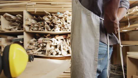 mid section of african american male carpenter wearing an apron in a carpentry shop