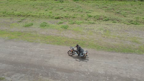 man practicing tricks on motorbike riding on dirt road in africa, aerial tracking shot