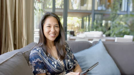 Happy-asian-woman-using-tablet-and-smiling-in-sunny-living-room,-slow-motion