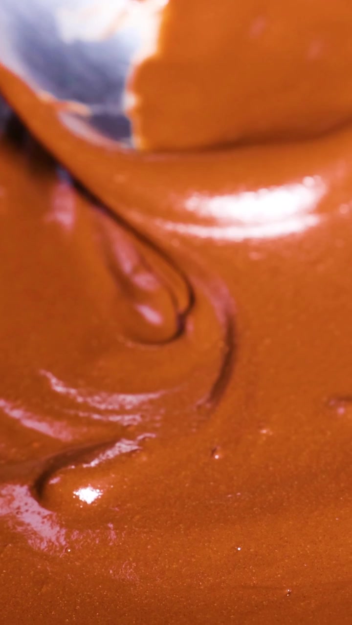 Extreme close-up of a silver spoon mixing rich, glossy melted chocolate with smooth swirls.