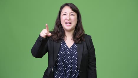 성숙 한 분노 한 아시아 사업가 여성 은 소리 지르면서 카메라 를 가리키고 있다
