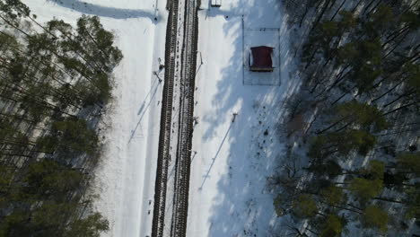 Ascend-aerial-top-view-of-snowy-rails-surrounded-by-pine-trees-in-winter-and-sunlight