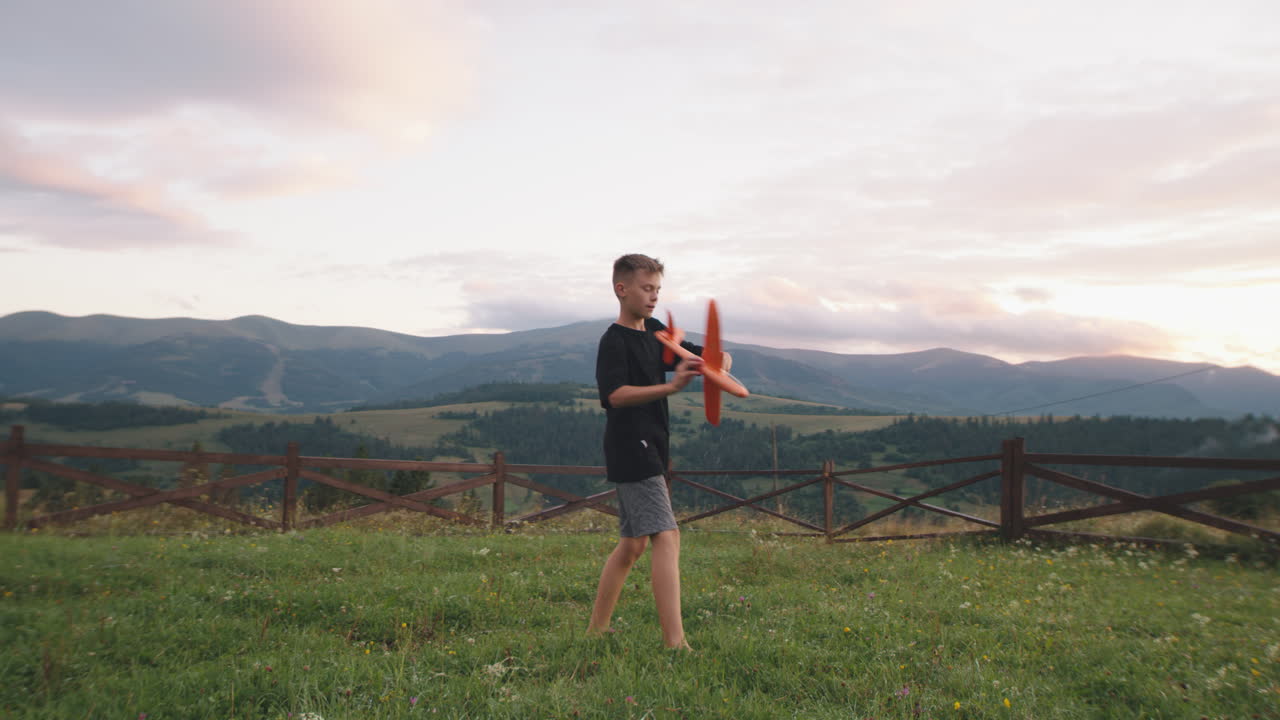 A Boy Playing With a Toy Airplane in a Mountain Field at Sunset