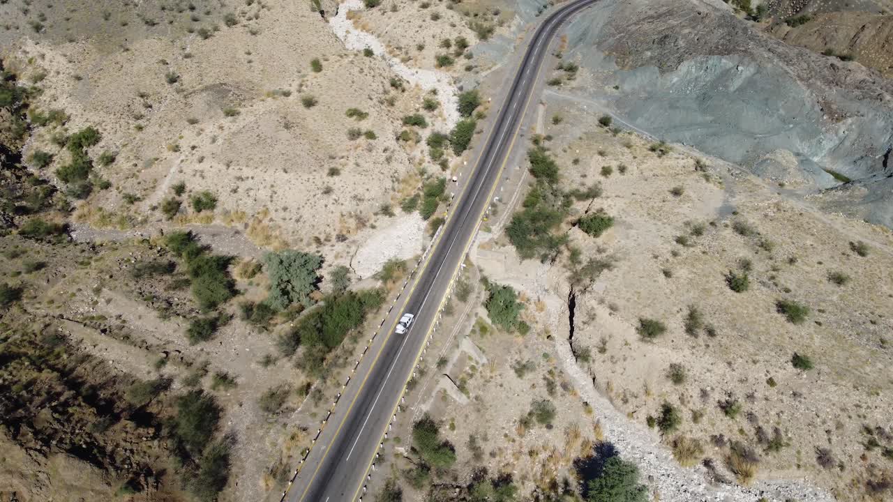 발로치스탄의 바위산 풍경에서 사막 고속도로를 따라 운전하는 자동차의 공중 드론 뷰