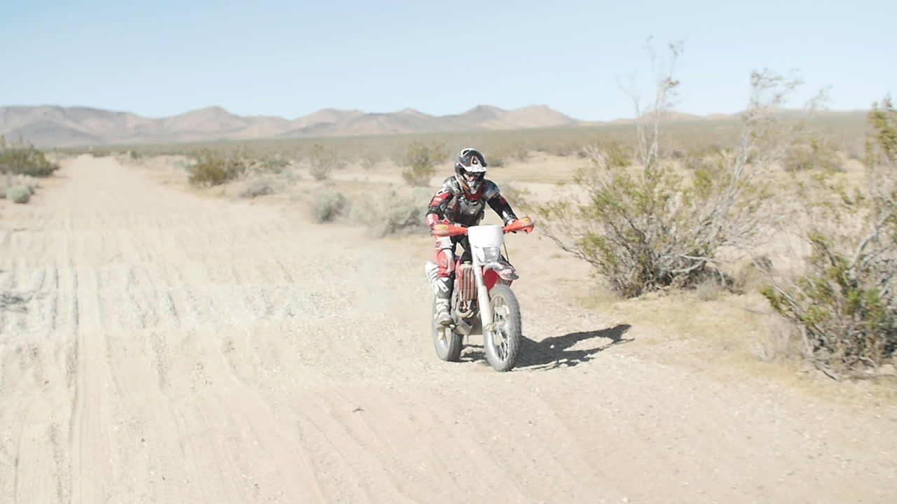 슬로우 모션: 더트 바이커가 자신의 crf 혼다를 타고 후프 섹션 위로 사막을 통과합니다.