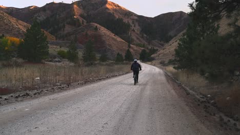 Frau-Fährt-Mountainbike-Auf-Unbefestigter-Forststraße-Bei-Sonnenuntergang-In-Den-Bergen-Am-Späten-Nachmittag-Vor-Sonnenuntergang-Für-Eine-Schöne-Freizeitaktivität-In-Der-Natu