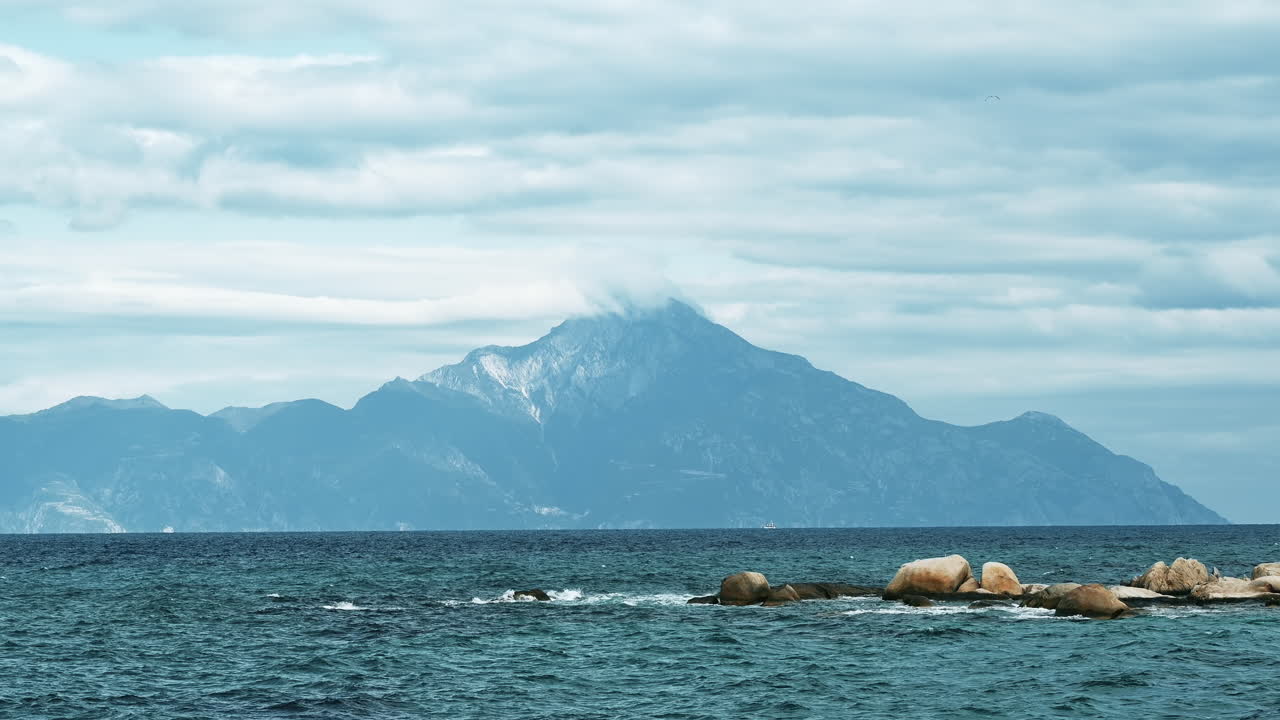 Mountain reaching clouds in the distance with Aegean sea on the foreground in Greece