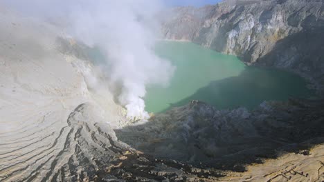 drone shot of white fog rising from sulfur mine with ijien acid lake at the background in java indonesia