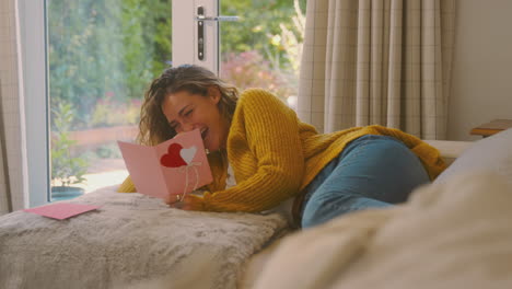 woman in cosy warm jumper lying on sofa at home lying on sofa reading romantic valentines day card