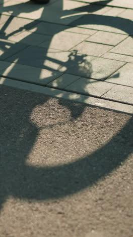 sombra de una bicicleta al revés proyectada en el suelo a medida que gira la rueda trasera, activada por alguien girando el pedal, creando un efecto de silueta dinámica bajo la cálida luz del sol en el pavimento