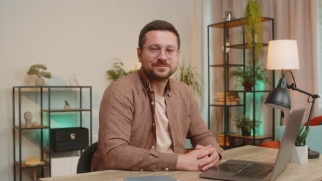 happy caucasian young man freelancer with laptop smiling at camera sitting at home office table
