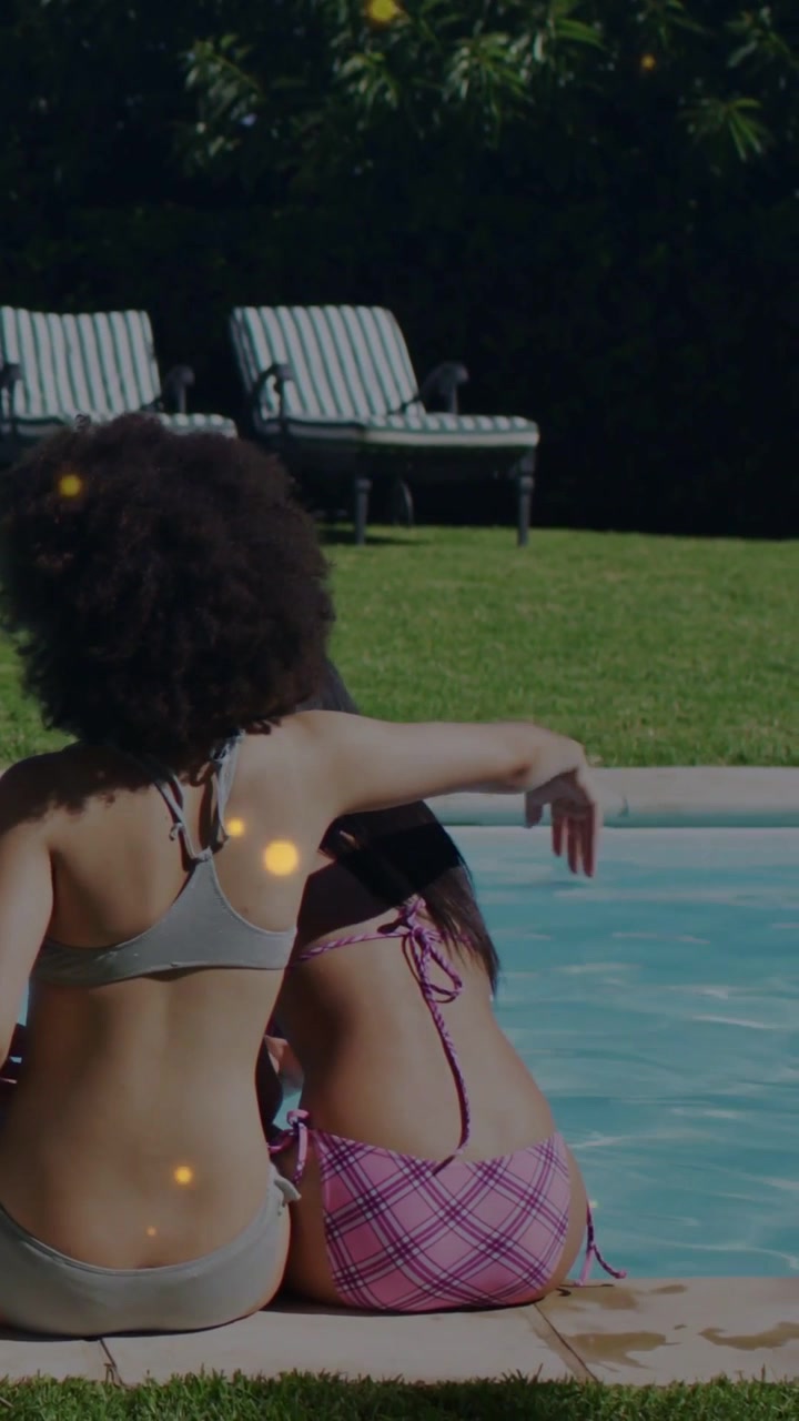 Vertikales Video: Linke Frau dreht sich, greift und legt den Arm um ihre Freundin am Pool, Bokeh-Effekt für entspannte Momente.