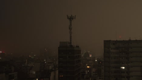 cell tower stands over buenos aires cityscape at night, surrounded by faint urban lights