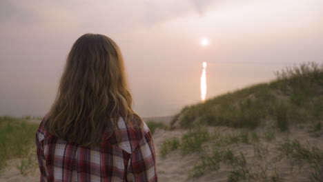 Handheld-shot-of-a-young-woman-standing-a-watching-the-sunset-over-a-large-body-of-water