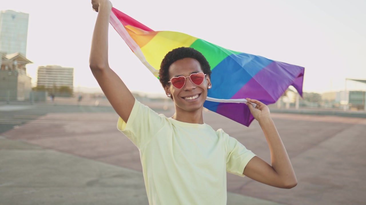 Smiling Young Man Holding Up a Vibrant Rainbow Pride Flag