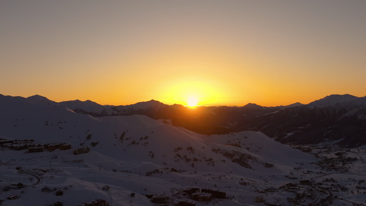Filmagem cinematográfica de drone 4K da estação de esqui de Gudauri durante um nascer do sol deslumbrante, apresentando tons suaves da hora dourada em encostas alpinas e terreno montanhoso acidentado. Gudauri_111