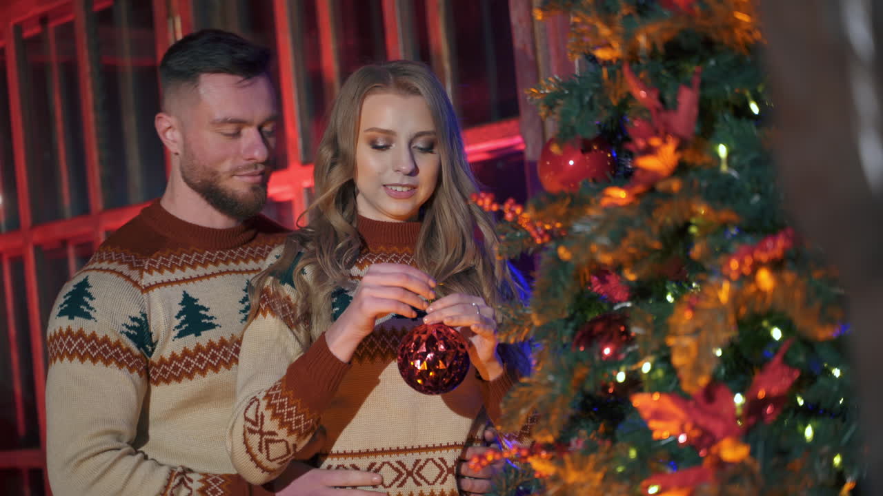Handsome man and beautiful woman decorate New year tree with christmas balls. Spanding holidays together.