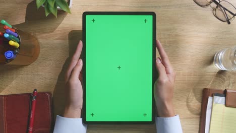 vista de arriba hacia abajo de una computadora portátil con pantalla verde simulada pantalla chromakey en un escritorio de oficina de madera al lado de la libreta con bolígrafos, gafas y un vaso de agua.